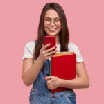 mujer-bonita-morena-sostiene-telefono-movil-envia-mensaje-texto-feliz-leer-comentarios-debajo-publicacion-sostiene-libro-texto_273609-25136 (1)